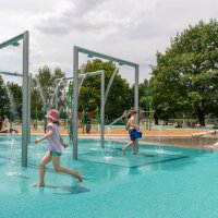 Kinder toben über einen Wasserspielplatz.